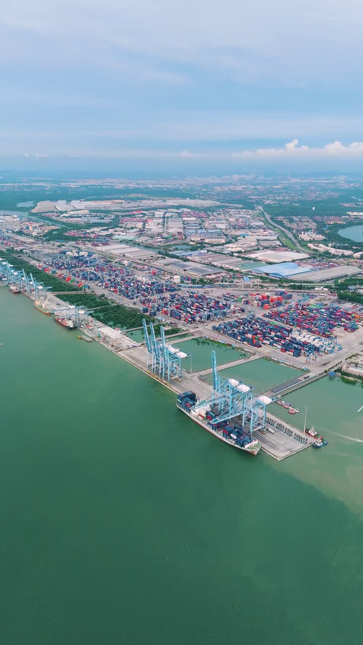 Vertical expansive drone shot of Northport in Klang, Malaysia, revealing container terminals, port infrastructure, and a sprawling cityscape under a partly cloudy sky.