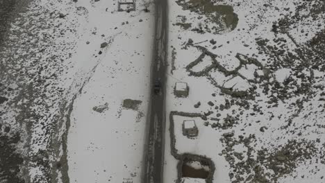 Vista-Aérea-De-Pájaro-Del-Camión-Negro-Que-Se-Acerca-Al-Puente-Sobre-El-Paisaje-Cubierto-De-Nieve-Del-Valle-De-Hunza