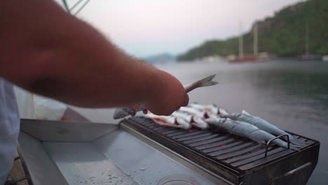 small whole gutted fish are placed onto outdoor grill on moored yacht