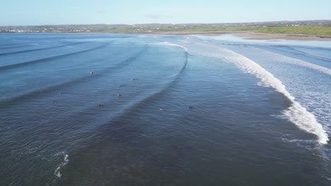 Luftaufnahme-über-Einer-Gruppe-Von-Surfern,-Die-Auf-Wellen-In-Der-Doughmore-Bay-Warten