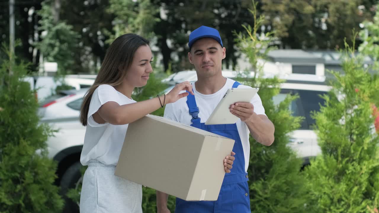 una mujer hermosa conoce a un repartidor que le da una caja de paquetes al lado de su casa, ella firma una firma electrónica en una tableta. concepto de mensajero, entrega a domicilio, compras en línea