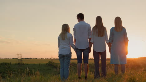 a group of friends enjoy the sunset over a picturesque valley. back view