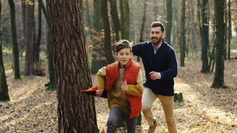 padre feliz caucásico con su pequeño hijo corriendo y jugando en el bosque