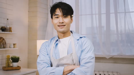 close up view of japanese man wearing apron looking and smiling at the camera in the kitchen