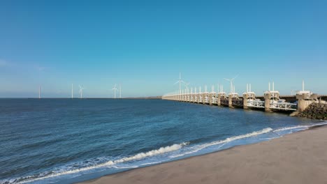 toma aérea de una playa vacía al lado de la barrera de marejada ciclónica del este de scheldt con turbinas eólicas en el horizonte en zelanda, los países bajos, en un hermoso día soleado