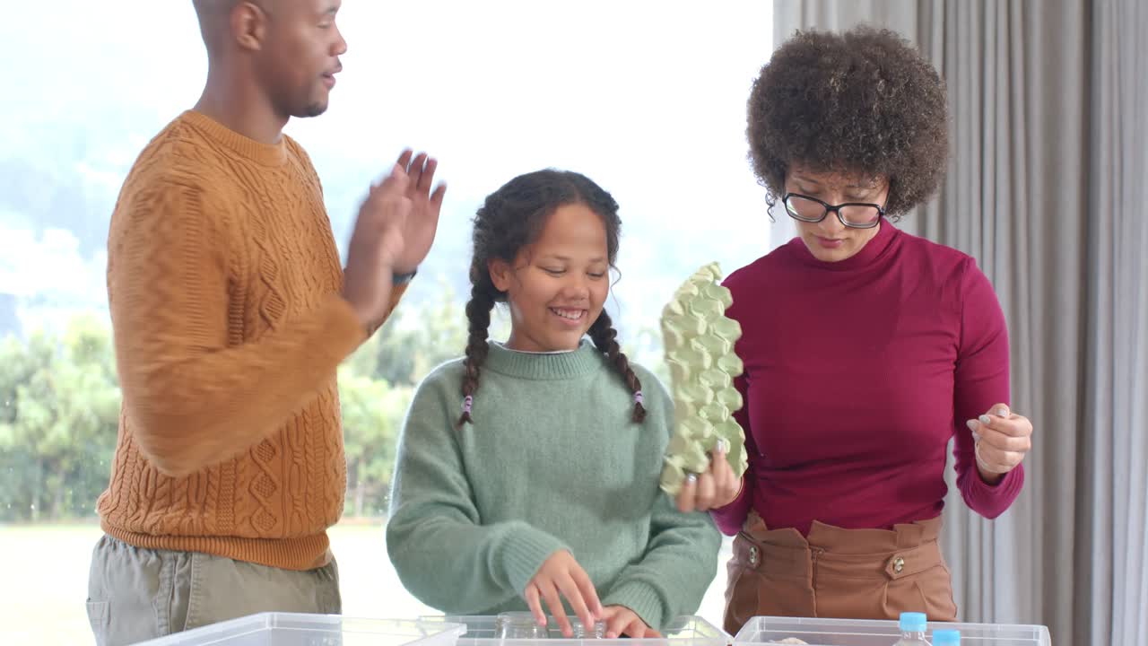 After father placing egg carton, diverse family sorting recyclables into bins at table by window