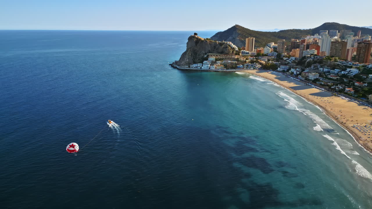 Aerial drone view of the buildings along the coastline with people parasailing in the sea in Benidorm, Spain in daylight