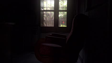 old armchair in a dark room in front of a windows through which the light enters