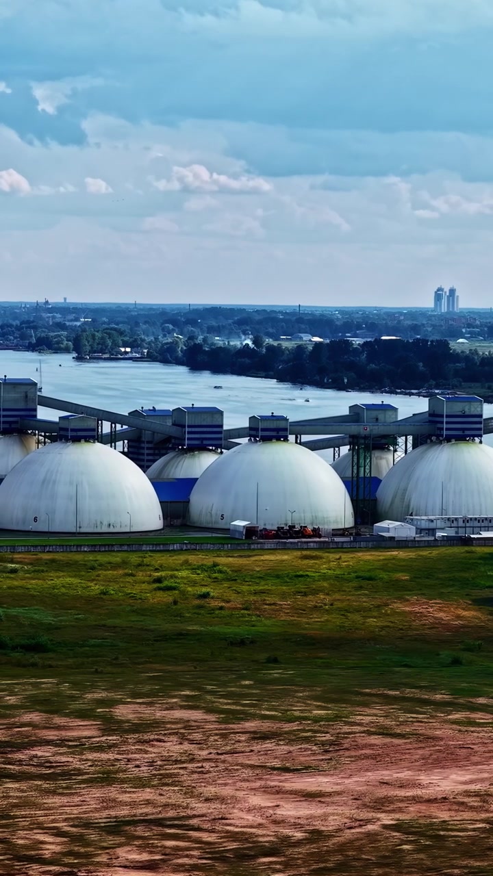 Una vista aérea de grandes cúpulas de almacenamiento industrial cerca de un río con una ciudad al fondo.