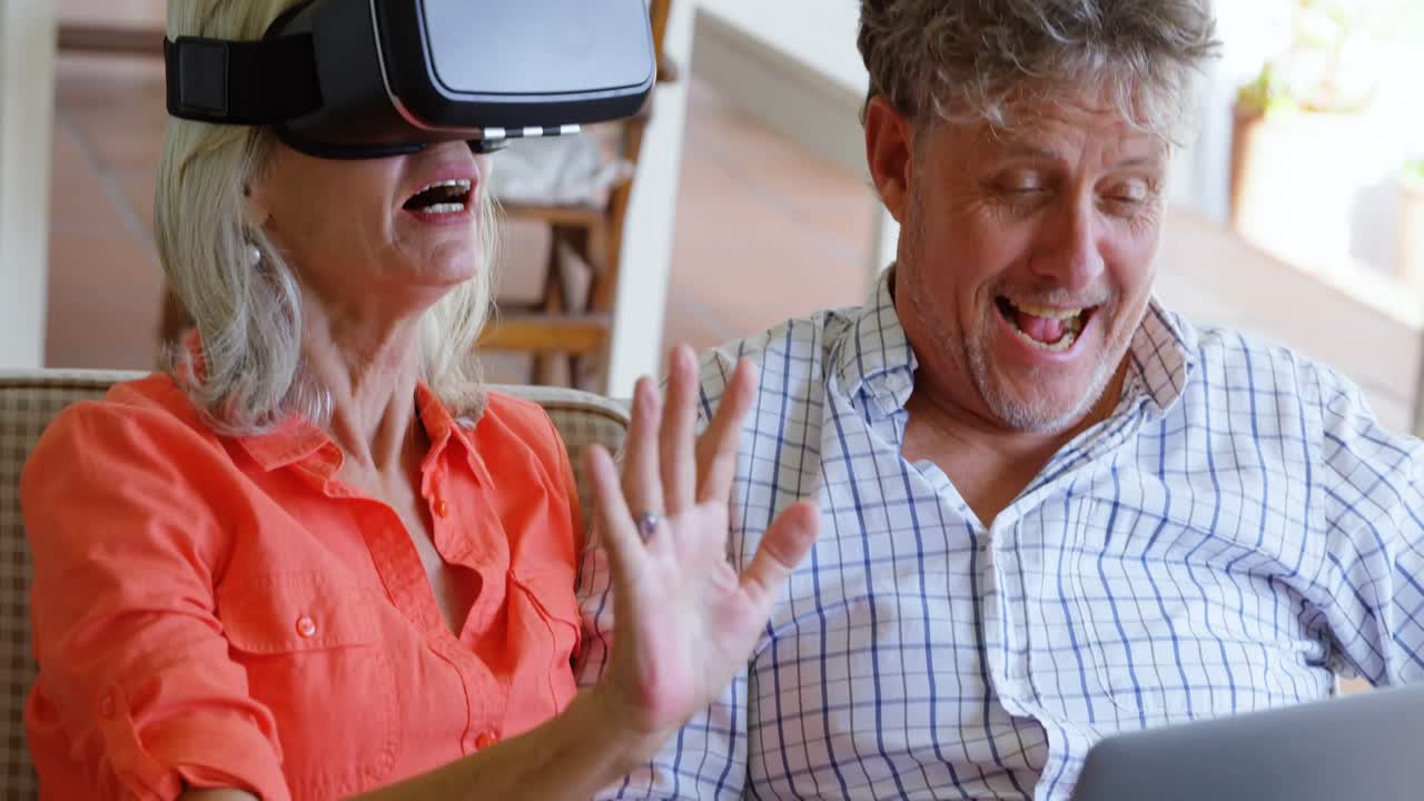 Coppia di anziani che usa laptop e visore VR sul divano 4k
