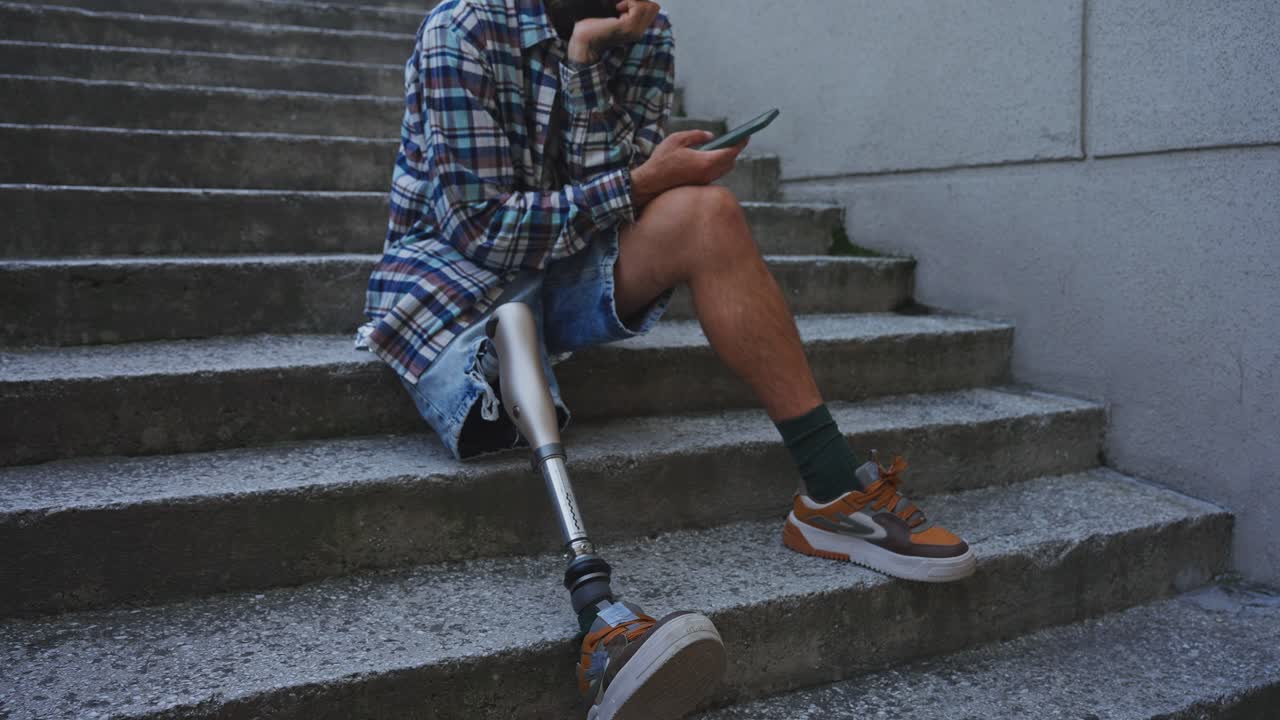 Man with prosthetic leg sitting on stairs using smartphone