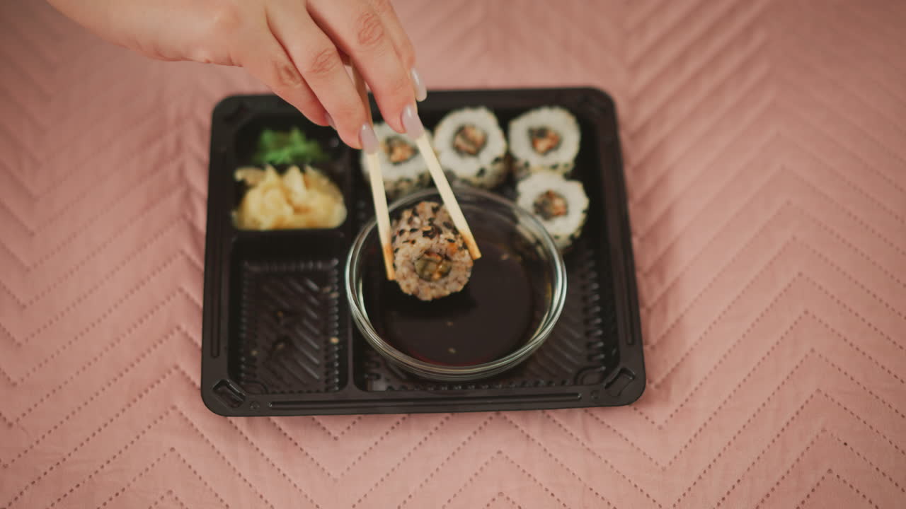 Hand using chopsticks to dip a piece of sushi in soy sauce
