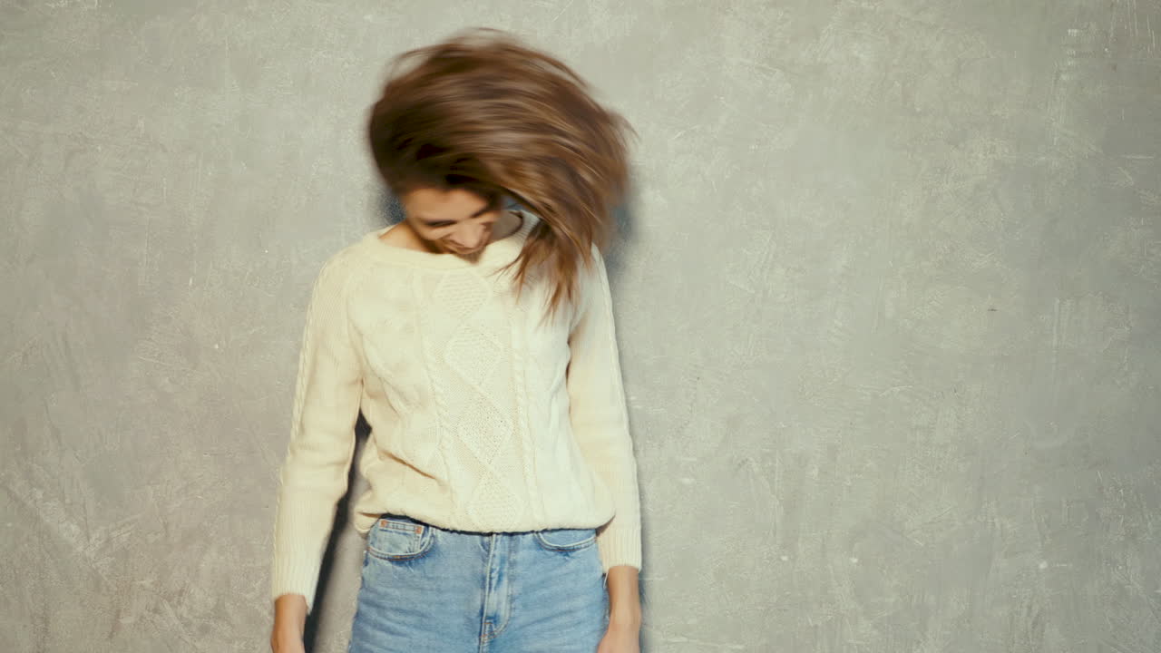 mujer con un suéter y vaqueros, con el cabello volando en el aire