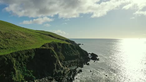 vista aérea de un acantilado marino desgastado a lo largo de la costa del cobre en el sur de irlanda con un barco en la luz solar reflectante