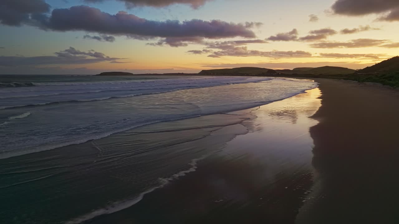 el cielo de gradiente rosado naranja se refleja a través de aguas poco profundas y olas de la curiosa bahía de la marsopa nueva zelanda