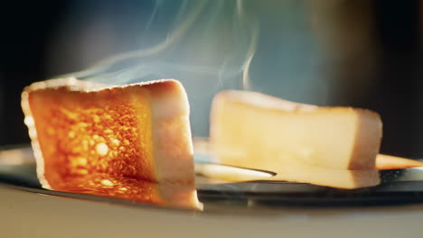 Zwei-Mit-Butter-Bestrichene-Croutons-Springen-Aus-Dem-Toaster,-Dampf-Entweicht-Aus-Dem-Heißen-Brot.-Die-Sonne-Vom-Fenster-Beleuchtet-Das-Essen-Wunderschön