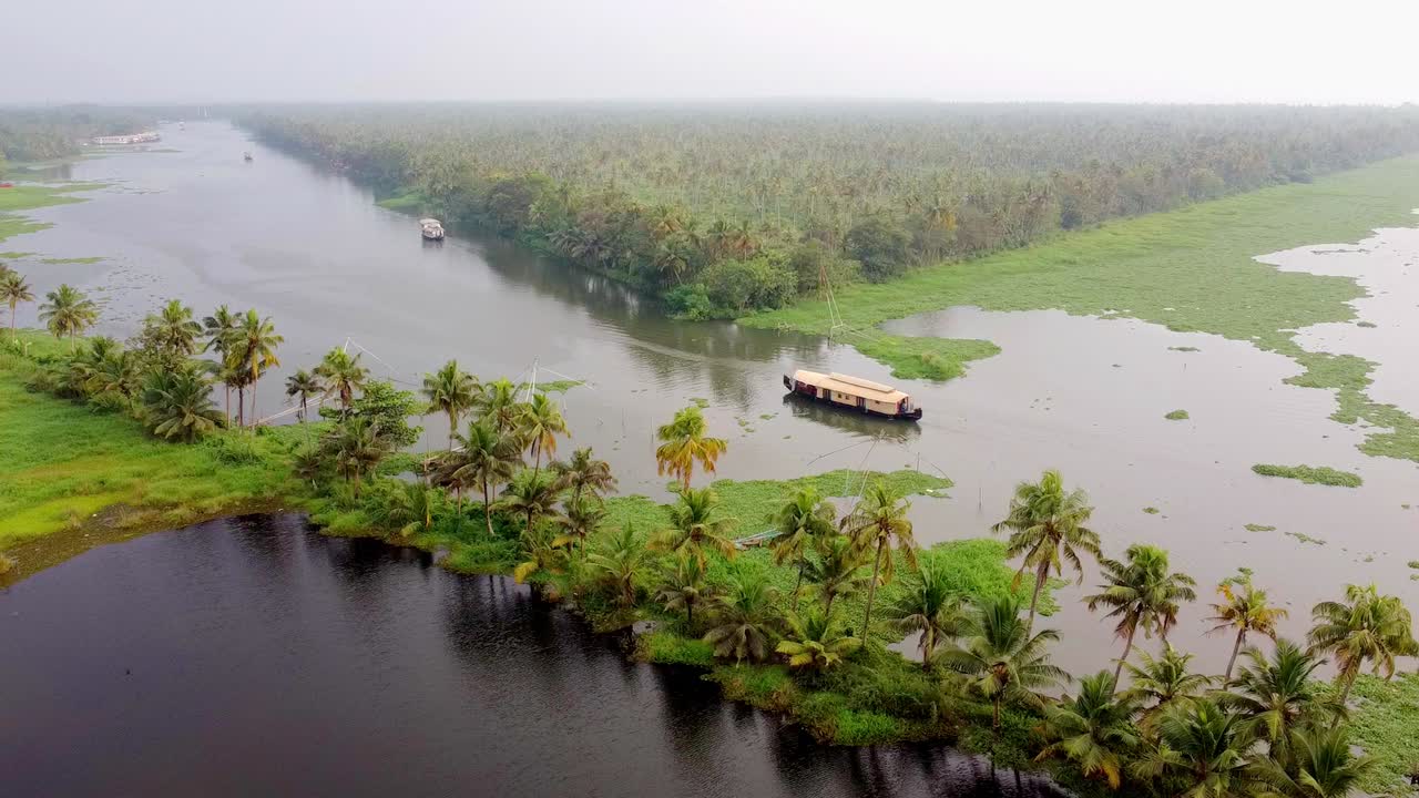 Ripresa aerea con drone di una lunga strada fiancheggiata da palme da cocco che conduce a una chiesa bianca in un lussureggiante paesaggio del Kerala con lagune