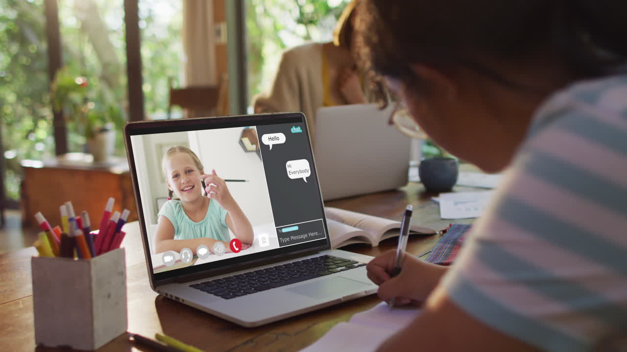Schoolgirl using laptop for online lesson at home, with school friend and web chat on screen