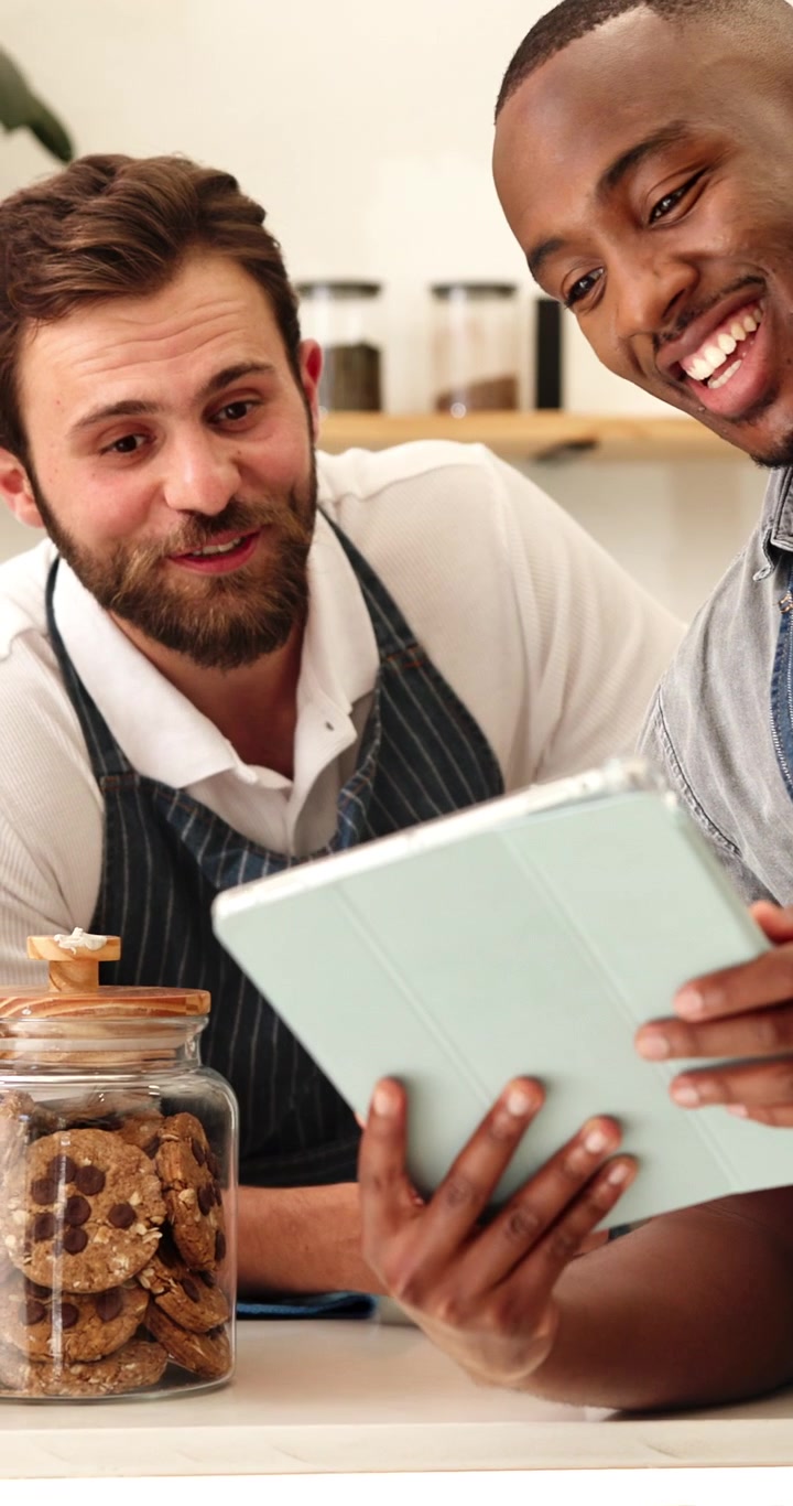 Two Male Baristas Discussing Orders on a Tablet in a Cafe