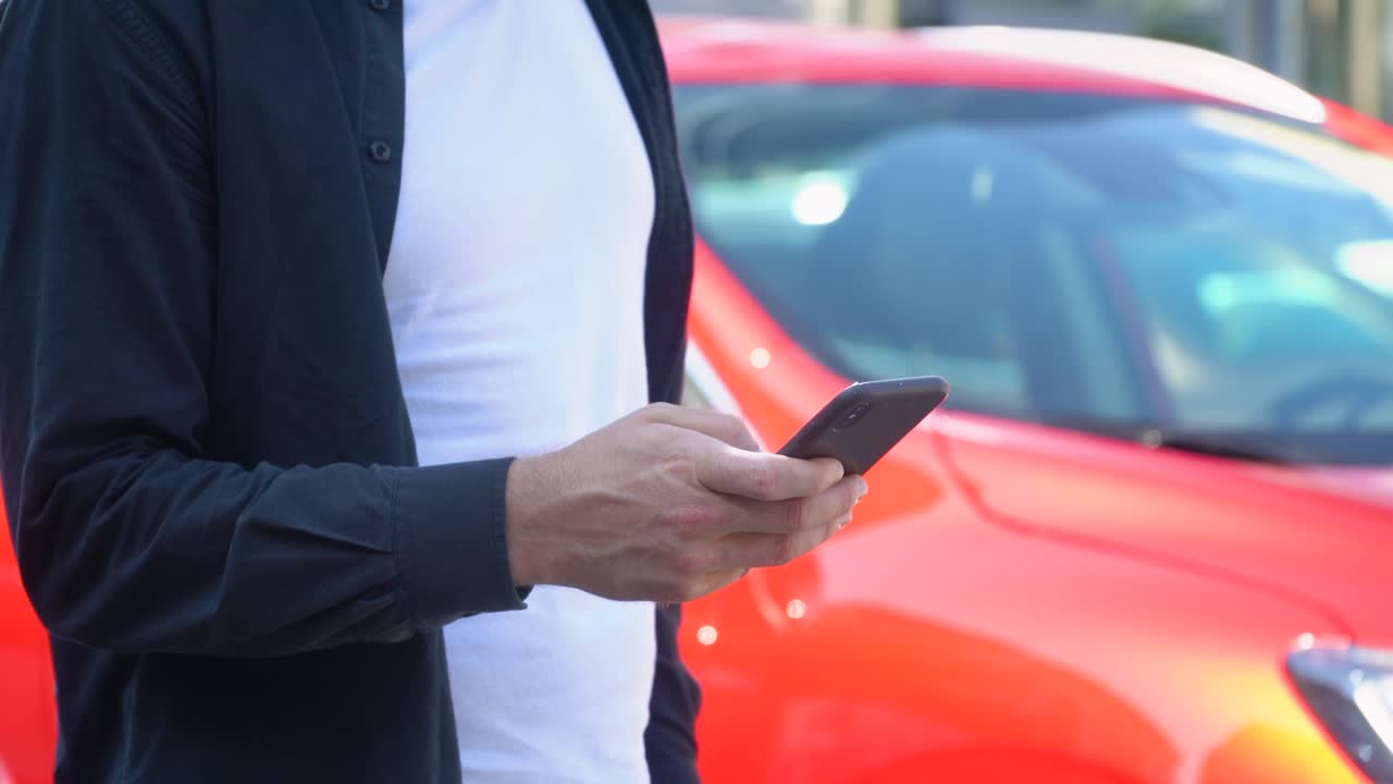 hombre confiado usando un teléfono inteligente cerca de un coche moderno. primer plano de un joven empresario usando su teléfono inteligente