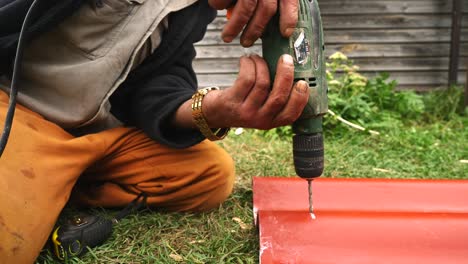 Man drilling a hole in metal roofing in a garden