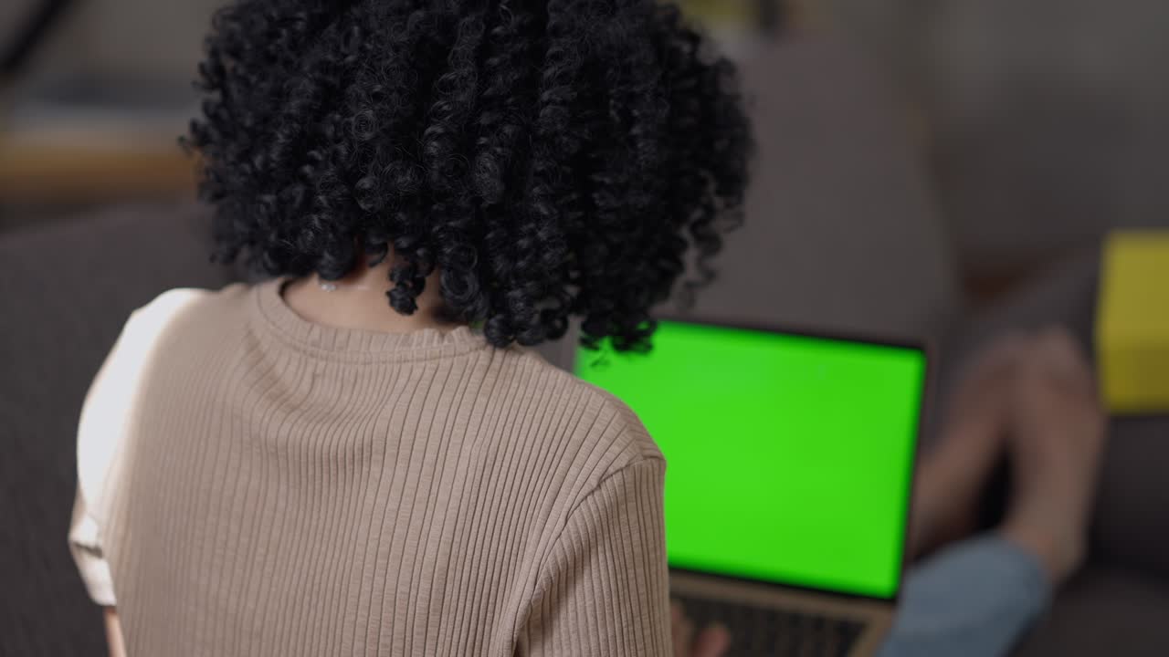 sparare sulla spalla di una giovane donna afroamericana che scrive sulla tastiera di un portatile chromakey. concentrato professionista sottile che lavora online in ufficio a casa surfando su internet messaggistica.