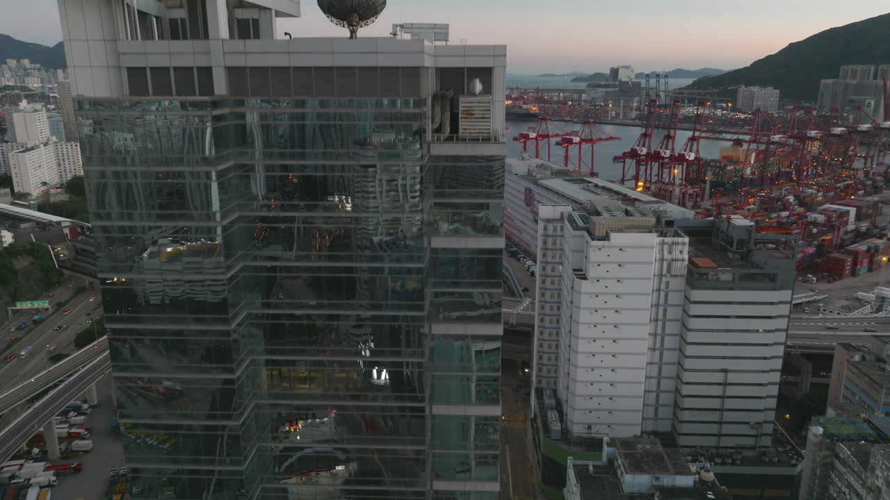 toma aérea de drones que se eleva sobre un edificio de vidrio que revela el puerto de envío en hong kong durante el amanecer