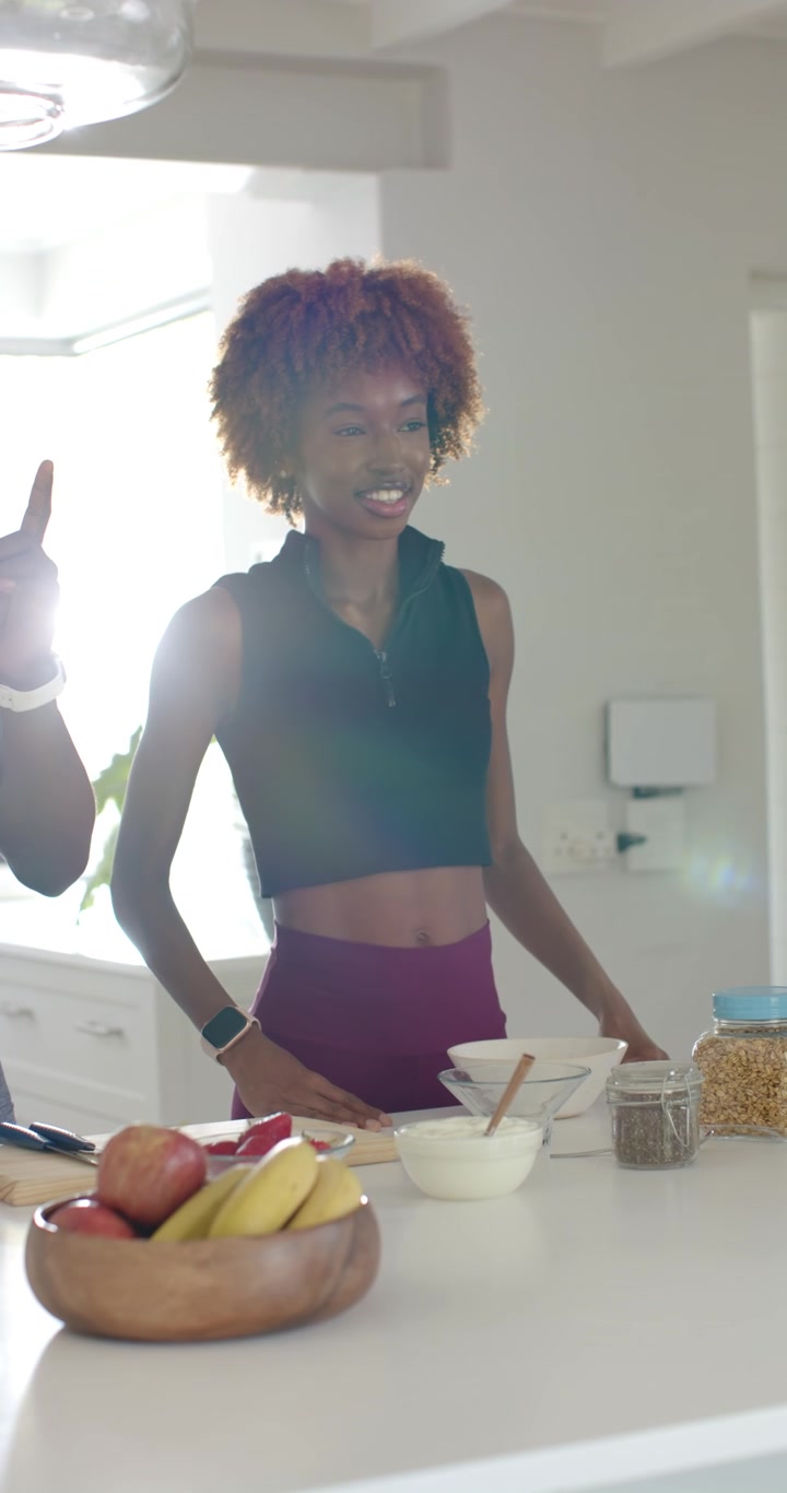 Video verticale: Coppia multietnica che cucina in cucina, l'uomo parla e indica le ciotole, la donna indossa un crop top.