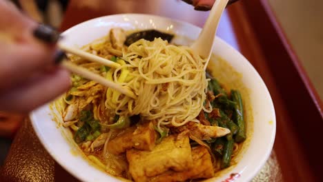 chopsticks lifting noodles from a soup bowl