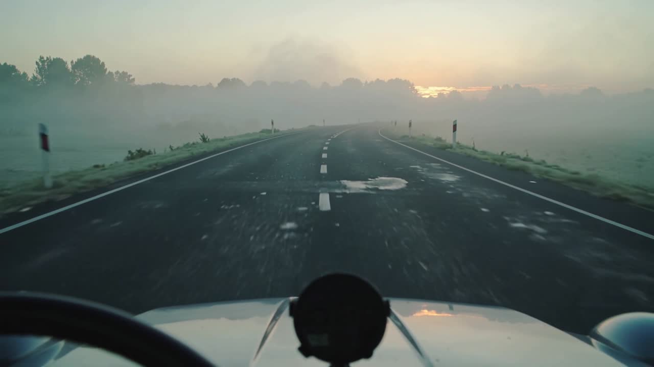 Telecamera montata sul cofano che filma la strada dopo l'avvio del motore lungo una strada rurale all'alba, con il cofano in vista.