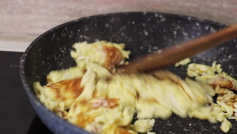 huevos revueltos dorados en una sartén negra con espátula de madera, de cerca