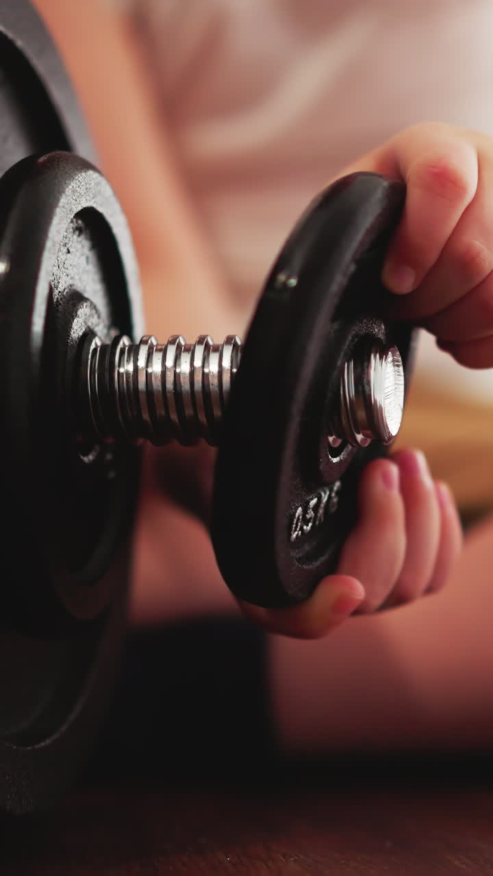 Curious toddler removes gear detail from heavy barbell with hands sitting on floor. Little boy studies weight equipment in gym closeup slow motion