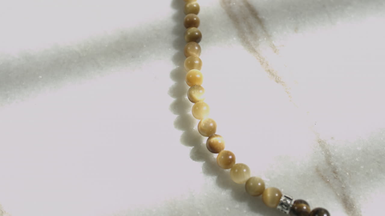 Carrellata di perle di Occhio di Tigre Giallo in una mala di preghiera posizionate su marmo bianco ripresa in UHD.