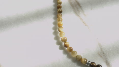 sliding shot of yellow tiger's eye beads in a prayer mala placed on white marble shot in uhd