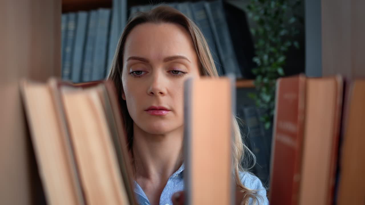 уверенная в себе блондинка выбирает старую бумажную книгу на полке шкафа в библиотеке.