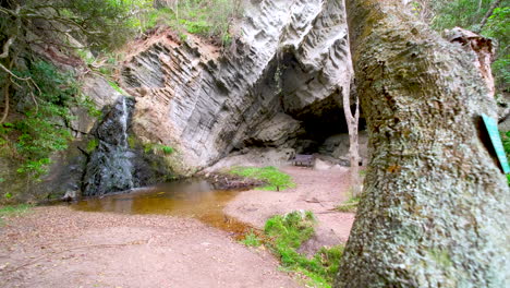 small jungle waterfall next to cave with seating area on trail to storms river