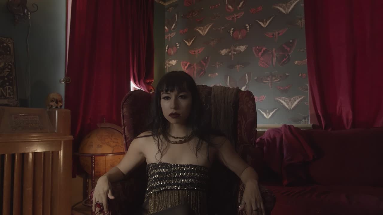 mujer gótica sentada en una silla de respaldo alto vintage pensativa en una habitación vintage