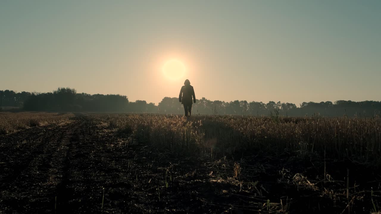 Um homem caminha por um campo queimado ao nascer e pôr do sol. Silhueta.