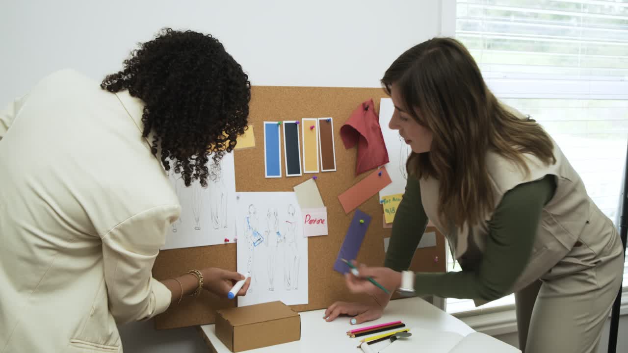 Two designers starting work at white table pinning sketch and arranging swatches to finalize layout