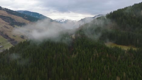 Misty-forested-mountains-with-snow-peaks-at-Saalbach-Hinterglemm-,-aerial-view