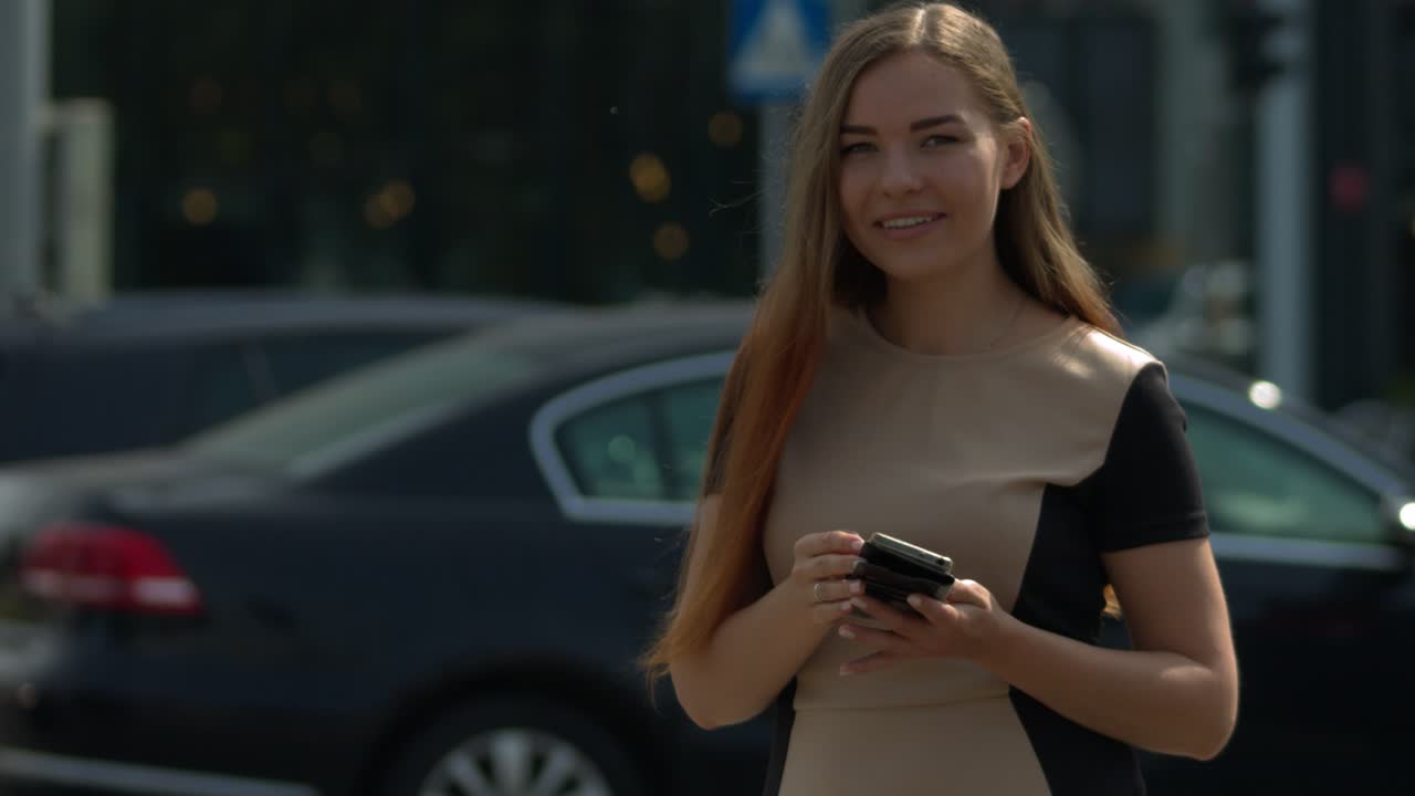 una hermosa joven en el centro de una gran ciudad al lado de una gran intersección de carreteras usa un teléfono inteligente