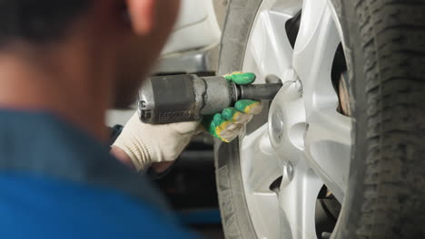 close-up head view of an engineer attentively watching a colleague using a pneumatic tool to tighten the bolt of a car in a garage, focus on precision, and professional automotive maintenance