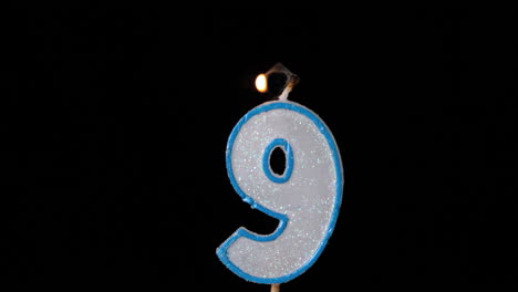 Nine-birthday-candle-flickering-and-extinguishing-on-black-background