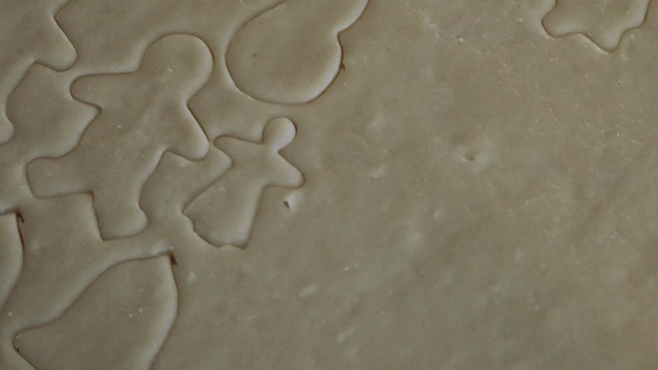 An extreme close up of an angel shaped cookie cutter being used to cut out a cookie in a sheet of holiday shaped cookies