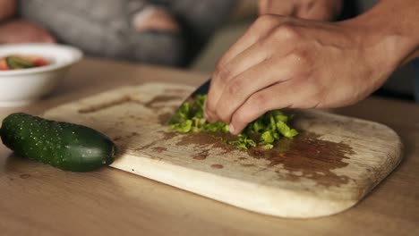 close up slow motion footage of a young mulatto guy cutting lettuce for salad, making lunch with his girlfriend who's sitting beside him on the kitchen table surface.