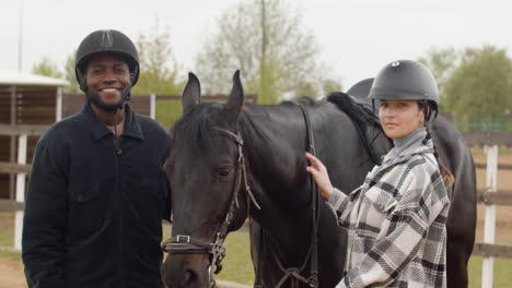 two friends petting black horse and looking at camera outdoors