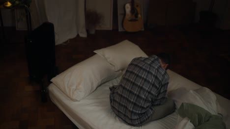 man sitting/lying on bed in dark bedroom