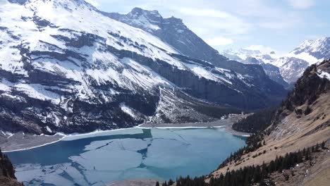 flight with a drone over a frozen lake in switzerland, mountains with snow in the background