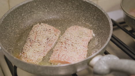 mano de mujer sosteniendo y moviendo la sartén con un delicioso salmón cocinado en la estufa