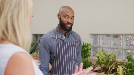 video of happy african american salesman showing organic vegetables to caucasian female customer